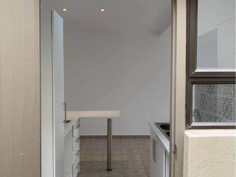 A view into a clean, empty kitchen featuring white built-in cabinetry, tiled flooring, and recessed lighting, accessed through an exterior doorway.