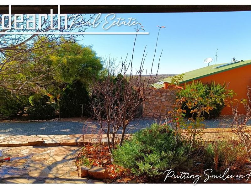 A view of the rear garden area featuring stone paving, established landscaping, and a stone boundary wall with a view of the adjacent property.