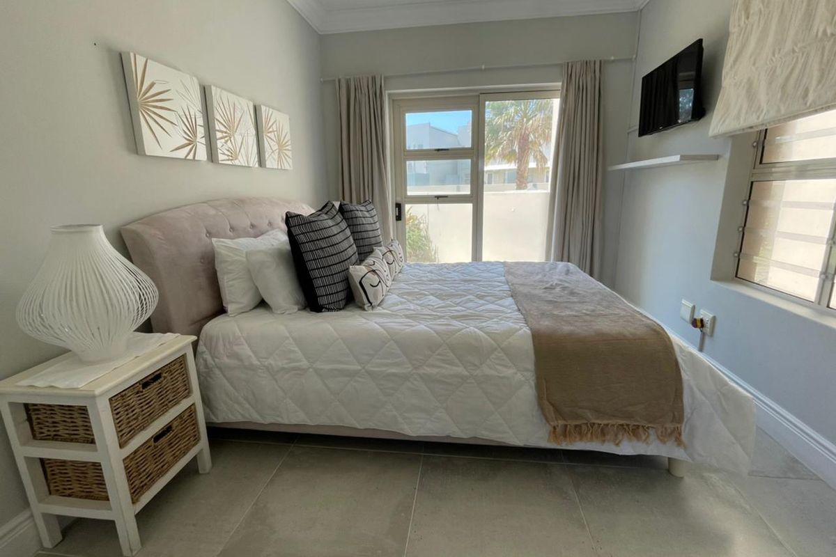 A well-maintained bedroom featuring neutral tiled flooring, crown molding, and a sliding glass door providing natural light and access to the exterior.