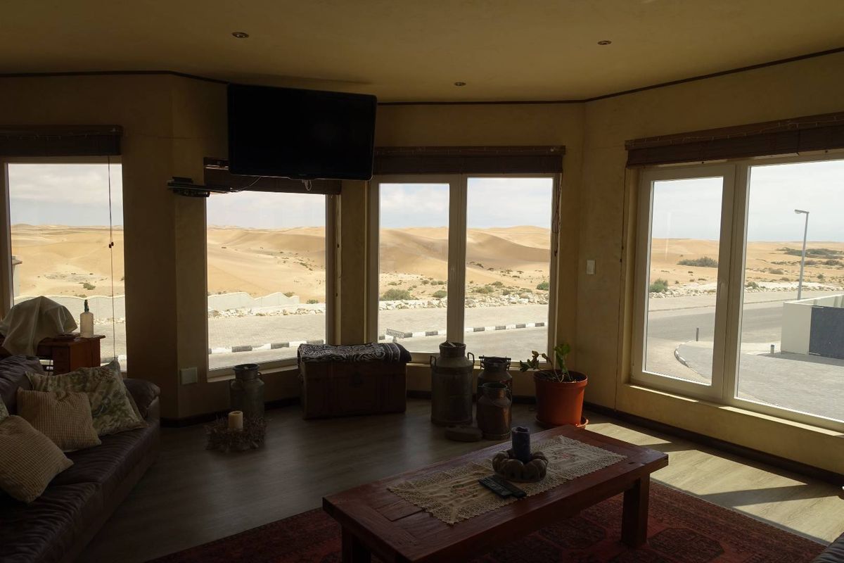 A living room featuring large windows with expansive desert views, recessed ceiling lighting, and wood-look flooring.