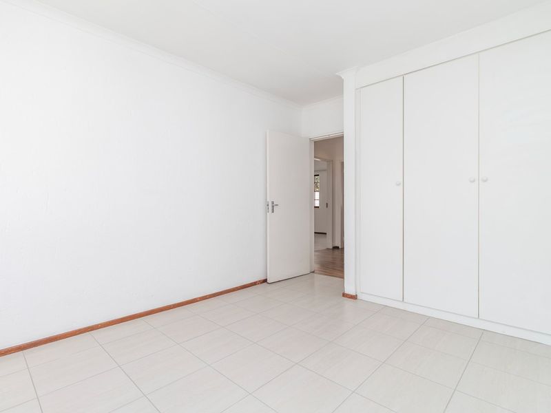 A bright, empty bedroom featuring neutral tiled flooring and ample built-in cupboard storage space.