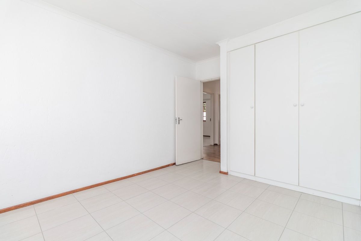 A bright, empty bedroom featuring neutral tiled flooring and ample built-in cupboard storage space.