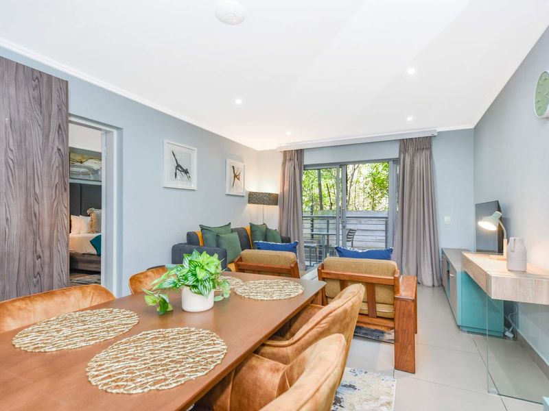 A bright open-plan living and dining area featuring tiled floors, recessed lighting, and a sliding glass door leading to an outdoor balcony.