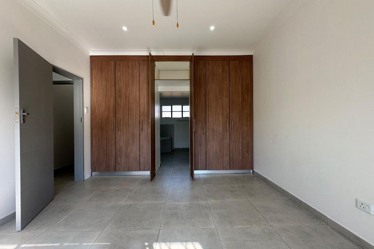 A spacious, empty bedroom featuring modern tiled flooring, built-in wooden cupboards, and a ceiling fan, offering a clean and neutral living space.