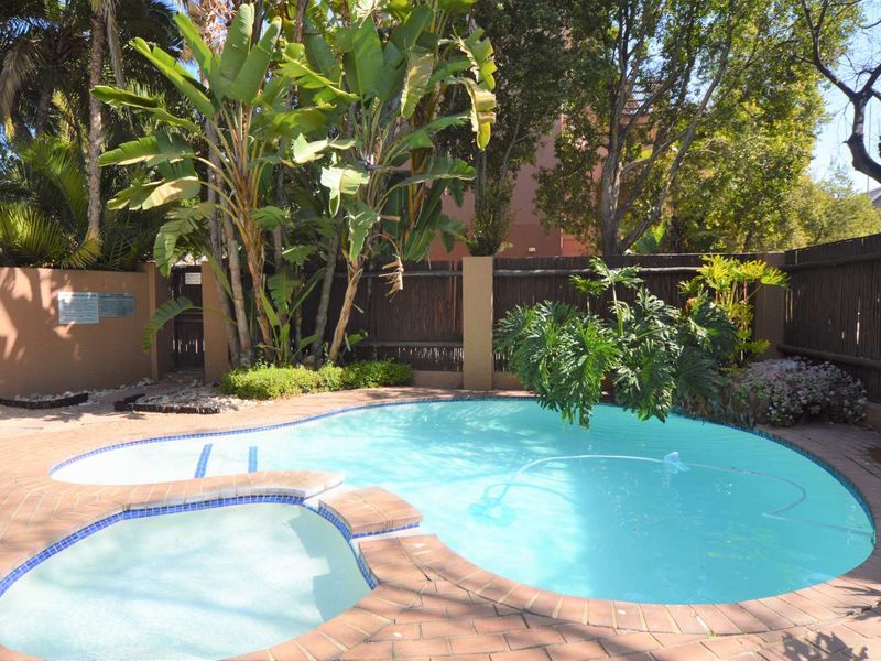 A well-maintained outdoor swimming pool area featuring an integrated spa, brick coping, and established garden landscaping with timber boundary fencing.