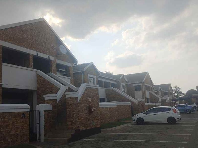 Exterior view of a multi-unit apartment complex featuring face brick facades, pitched roofs, and dedicated paved parking bays.