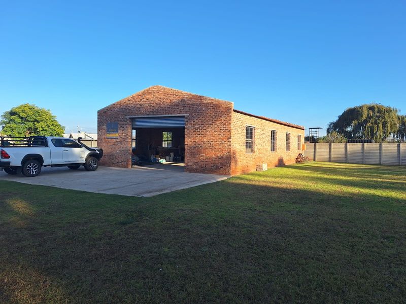 Industrial building featuring exposed brick construction, a large roller shutter door, and a concrete driveway, set on a spacious grassed lot.