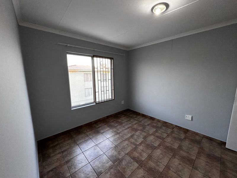 An empty bedroom featuring tiled flooring, a sliding window with security bars, and neutral grey walls.