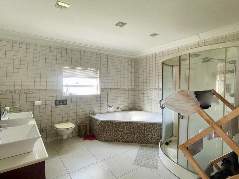 Spacious bathroom featuring a double vanity, corner bathtub, and a curved glass shower enclosure with tiled finishes throughout.