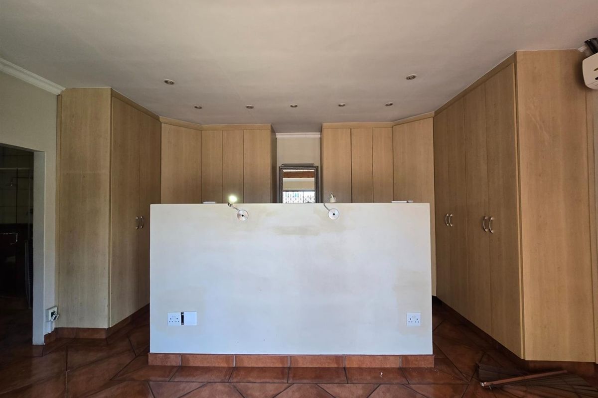 Spacious bedroom featuring extensive built-in wooden cabinetry, recessed ceiling lighting, and tiled flooring with a central partition wall.