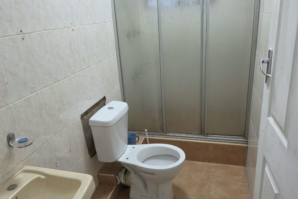 A compact bathroom featuring a toilet, shower enclosure, and washbasin, currently requiring maintenance to the tiled wall area behind the toilet.