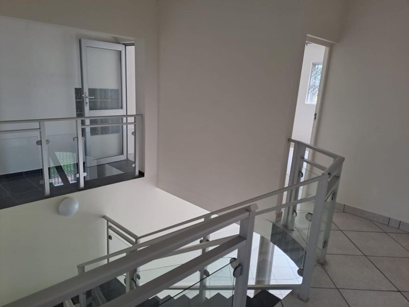 A bright, modern upper-level landing area featuring a glass balustrade staircase and neutral tiled flooring, providing access to multiple rooms.