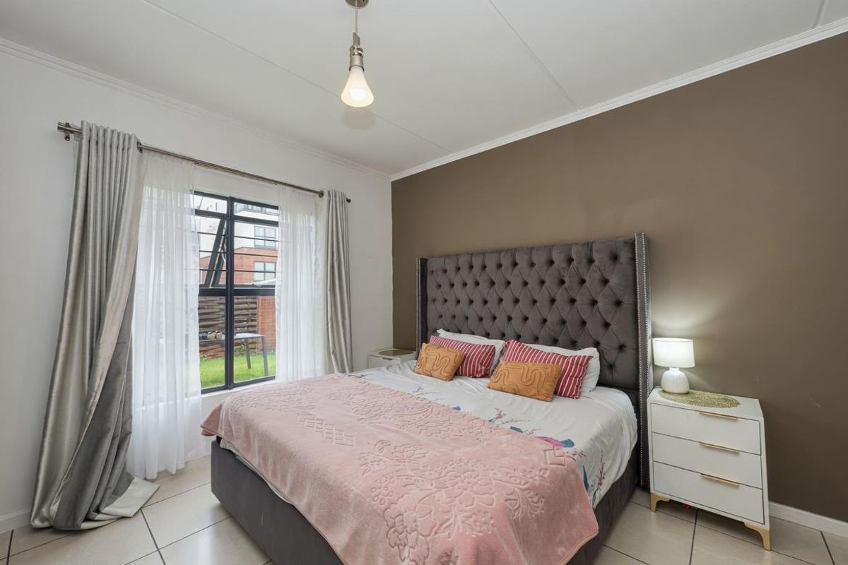 A well-maintained bedroom featuring neutral tiled flooring, a large casement window providing natural light, and a feature accent wall.