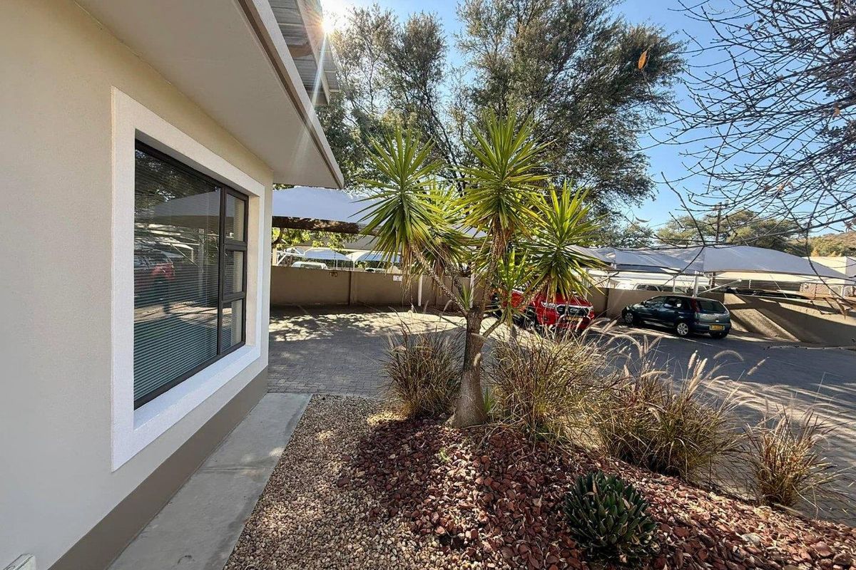 Exterior view of the office property showing a paved parking area with shade cloth carports and landscaped garden beds.