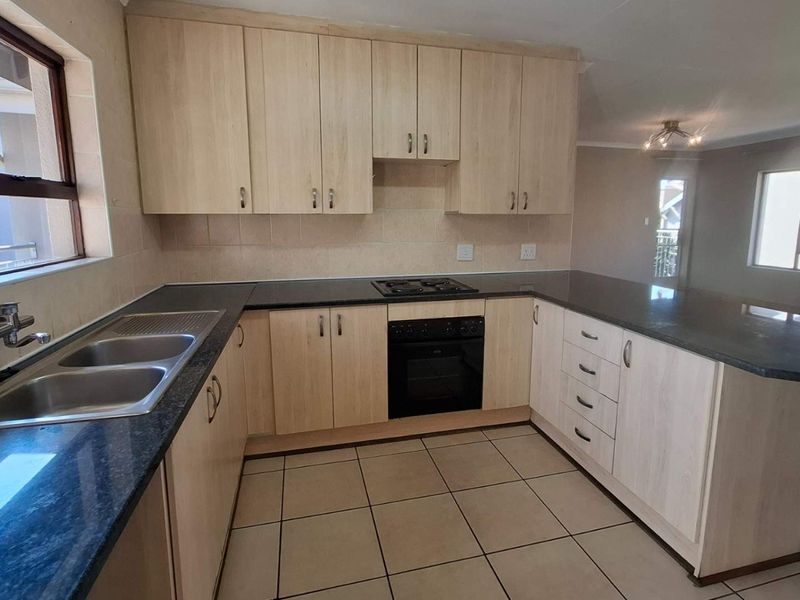 A functional kitchen featuring light wood cabinetry, dark granite countertops, a built-in oven and hob, and tiled flooring in an open-plan layout.