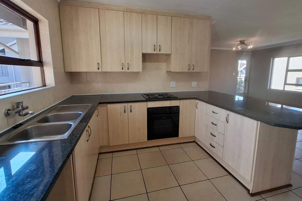 A functional kitchen featuring light wood cabinetry, dark granite countertops, a built-in oven and hob, and tiled flooring in an open-plan layout.