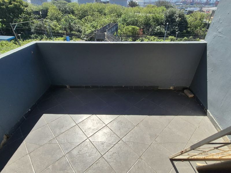 An open-air balcony featuring dark tiled flooring and a solid masonry balustrade, offering an elevated view of the surrounding greenery.