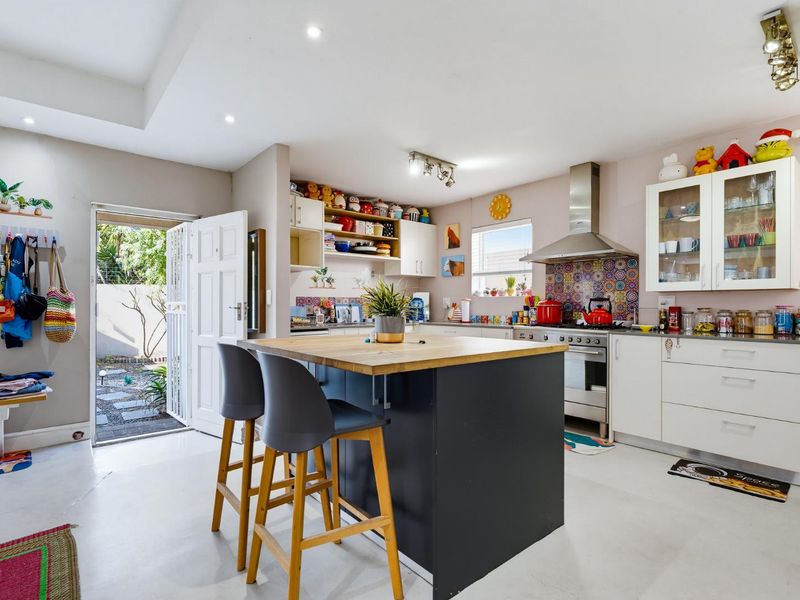 A bright kitchen featuring a central island with a wooden countertop, stainless steel stove, extractor fan, and ample built-in cabinetry with a decorative tiled backsplash.