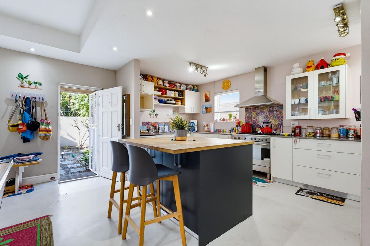 A bright kitchen featuring a central island with a wooden countertop, stainless steel stove, extractor fan, and ample built-in cabinetry with a decorative tiled backsplash.