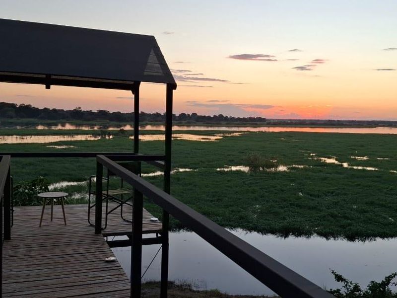 An elevated timber viewing deck with a metal frame canopy, offering expansive views over the surrounding wetlands at sunset.