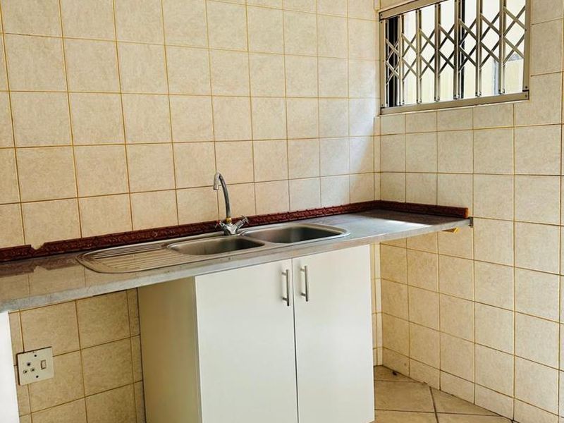 A functional scullery area featuring a stainless steel double sink, built-in base cabinetry, and tiled finishes throughout.