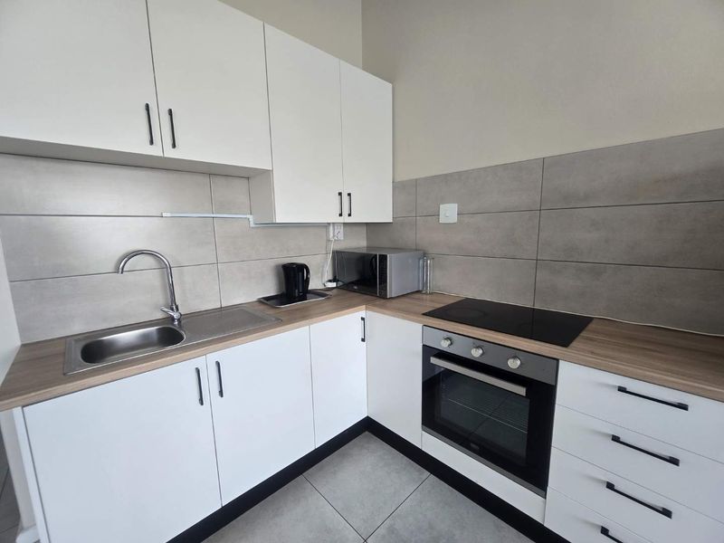 Modern kitchen featuring white cabinetry, wood-look laminate countertops, stainless steel sink, and integrated oven with ceramic hob.