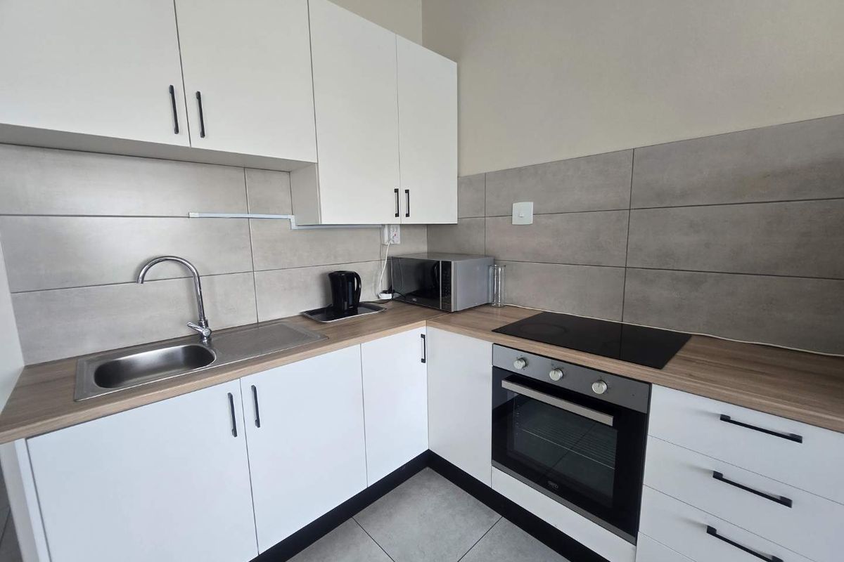 Modern kitchen featuring white cabinetry, wood-look laminate countertops, stainless steel sink, and integrated oven with ceramic hob.