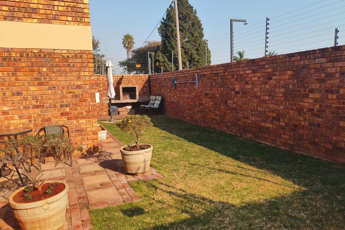 A private rear garden featuring a paved patio area, a built-in braai, and secure perimeter walling with electric fencing.