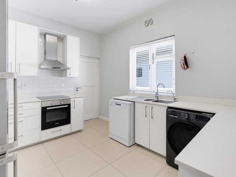 A clean, modern kitchen featuring white cabinetry, subway tile backsplash, integrated oven and hob, and dedicated space for laundry and dishwasher appliances.