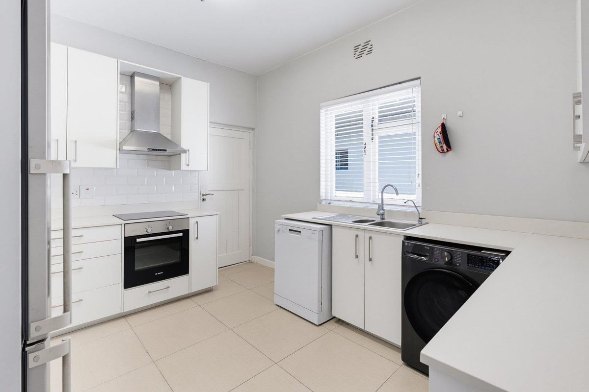 A clean, modern kitchen featuring white cabinetry, subway tile backsplash, integrated oven and hob, and dedicated space for laundry and dishwasher appliances.