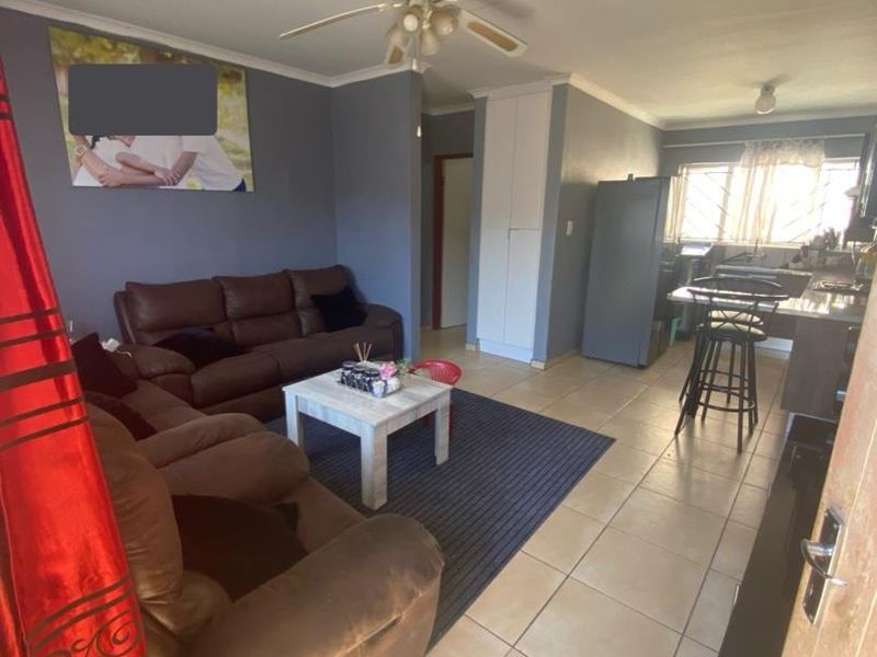 Open-plan living and kitchen area featuring tiled flooring, a ceiling fan, and built-in storage cupboards.