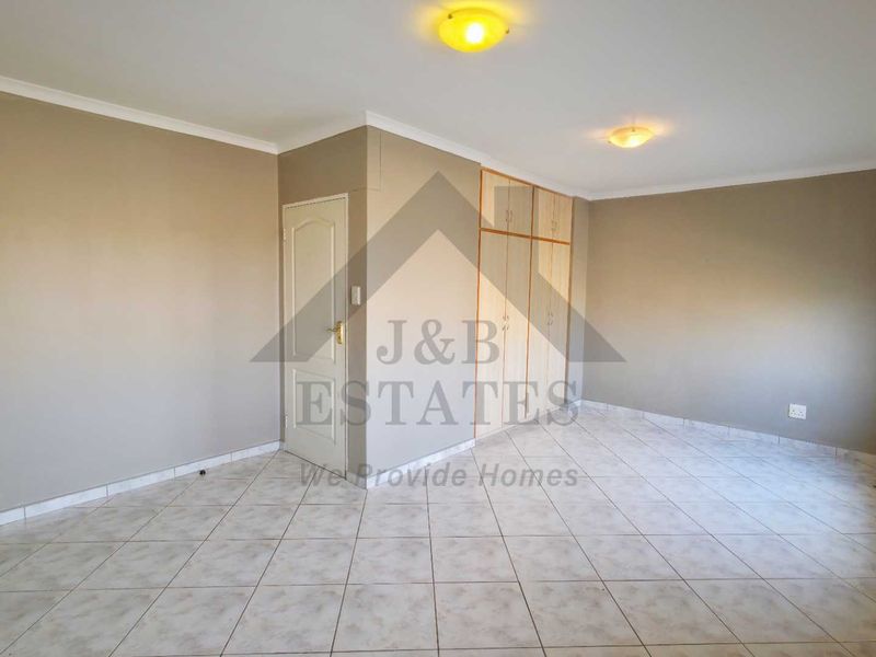 A spacious, empty bedroom featuring neutral walls, tiled flooring, and built-in cupboards, offering a clean canvas for personalization.