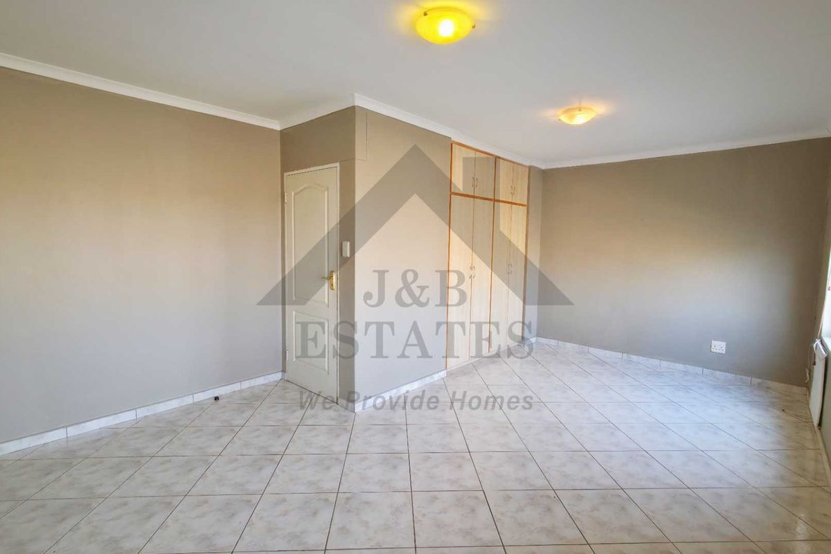 A spacious, empty bedroom featuring neutral walls, tiled flooring, and built-in cupboards, offering a clean canvas for personalization.