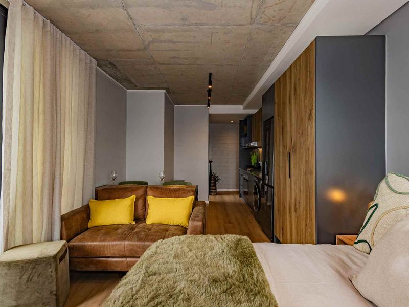 Modern open-plan studio apartment featuring an exposed concrete ceiling, sleek built-in cabinetry, and integrated kitchen appliances with high-quality finishes throughout.