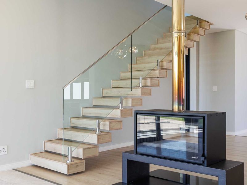 Modern living area featuring a contemporary floating staircase with glass balustrade and a sleek freestanding fireplace with a metallic flue.