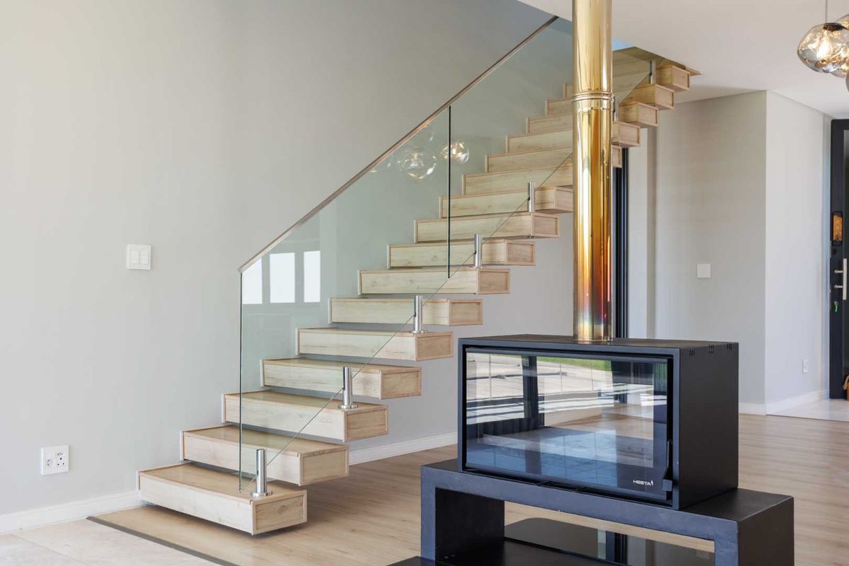 Modern living area featuring a contemporary floating staircase with glass balustrade and a sleek freestanding fireplace with a metallic flue.