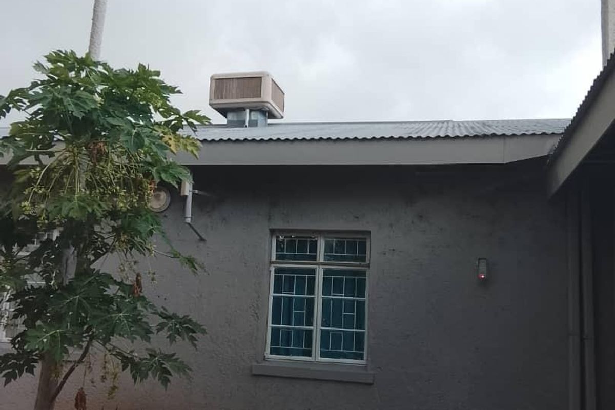 Rear exterior view of the house featuring a corrugated metal roof, an evaporative cooling unit, and a paved patio area.