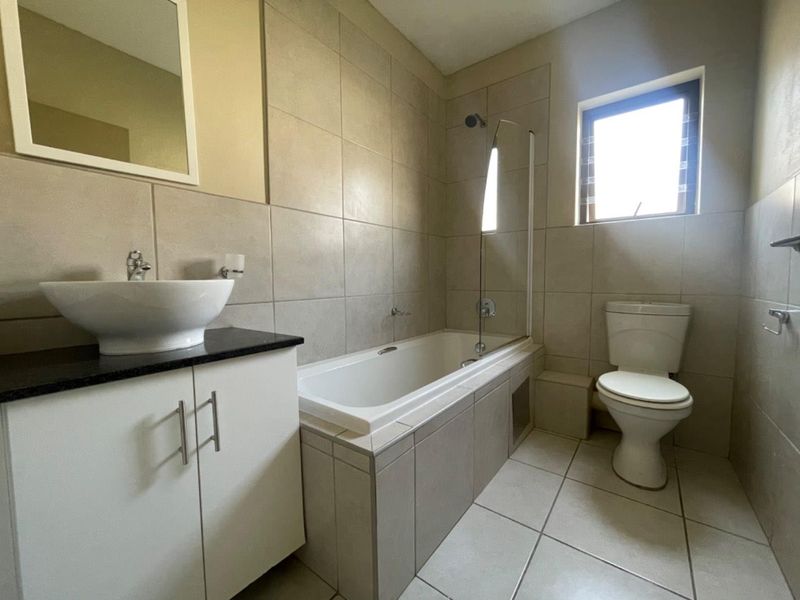 A clean, modern bathroom featuring a vessel sink on a granite vanity, a built-in bathtub with a glass screen, and neutral floor-to-ceiling tiling.
