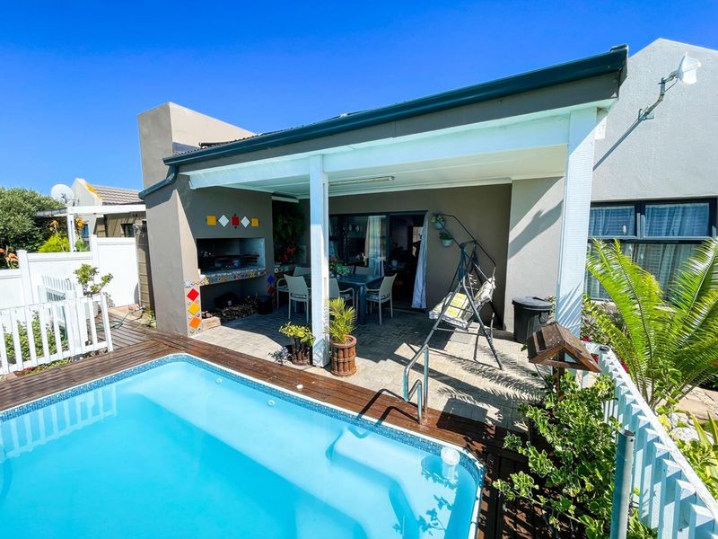 Outdoor entertainment area featuring a swimming pool, timber decking, and a covered patio with a built-in braai.