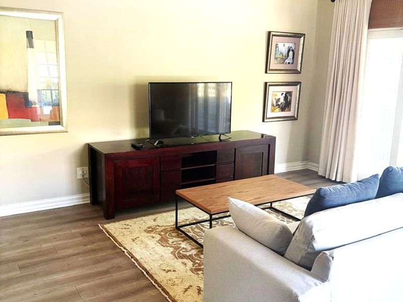 A bright living room featuring vaulted ceilings with exposed beams, modern laminate flooring, and a sliding glass door providing access to the outdoors.