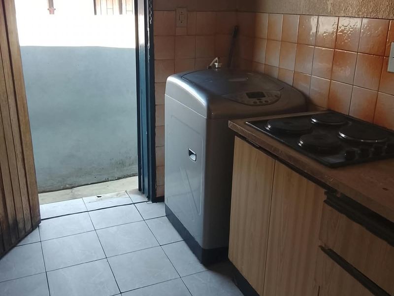 Compact scullery area featuring built-in cabinetry, an electric hob, and tiled finishes, with direct access to an outdoor space.