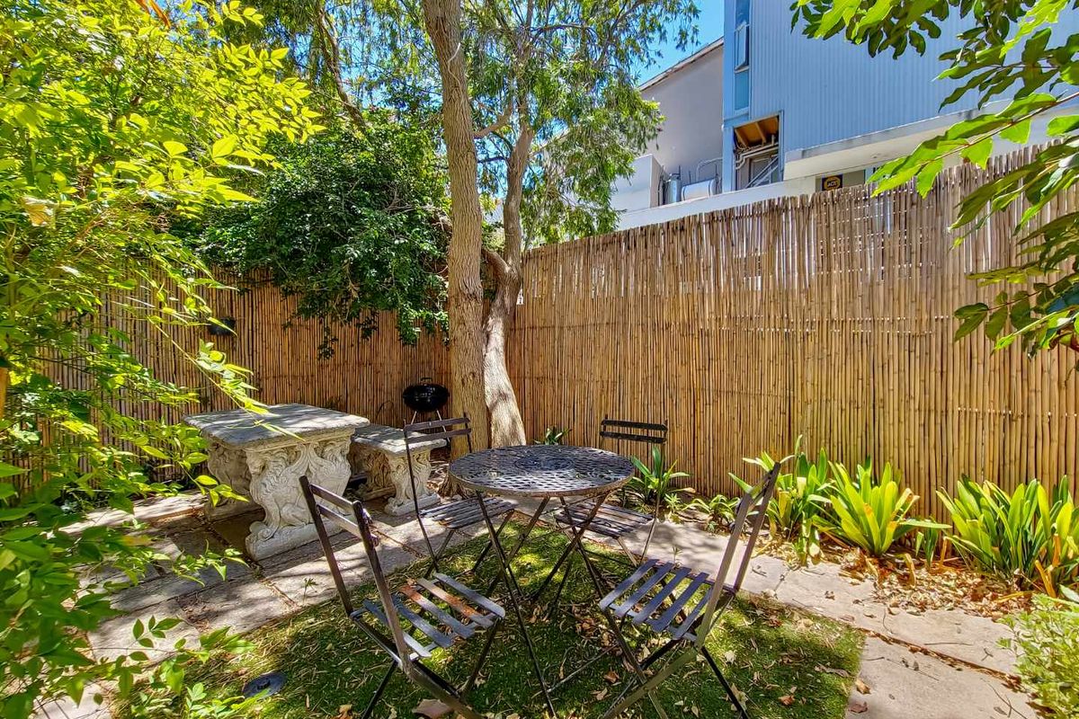 A private rear garden area featuring bamboo fencing, mature trees, and stone paving, providing a secluded outdoor space.