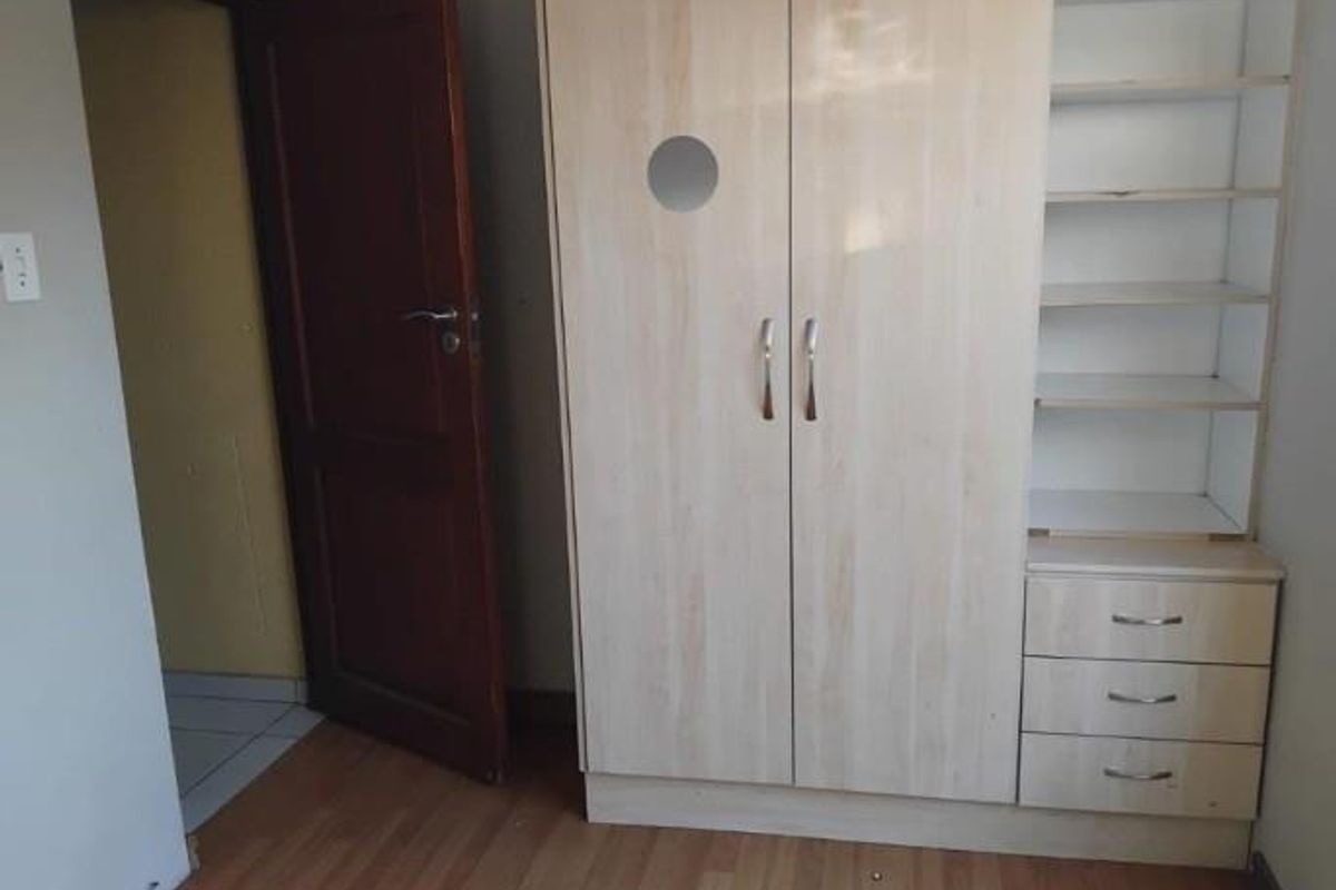 A bedroom featuring light wood-finish built-in cabinetry with integrated shelving and drawers, complemented by laminate flooring and a solid timber door.