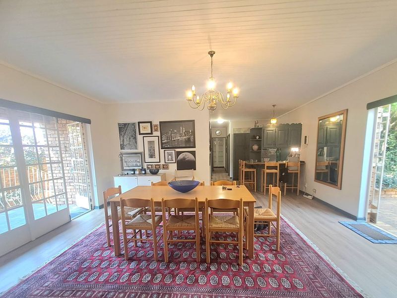 Spacious open-plan dining and kitchen area featuring timber-look flooring, direct access to outdoor patio spaces, and a functional breakfast bar.