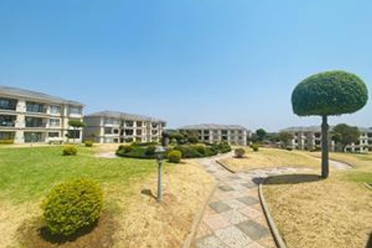 A view of the apartment complex grounds featuring landscaped gardens, paved walkways, and multi-story residential buildings under a clear blue sky.