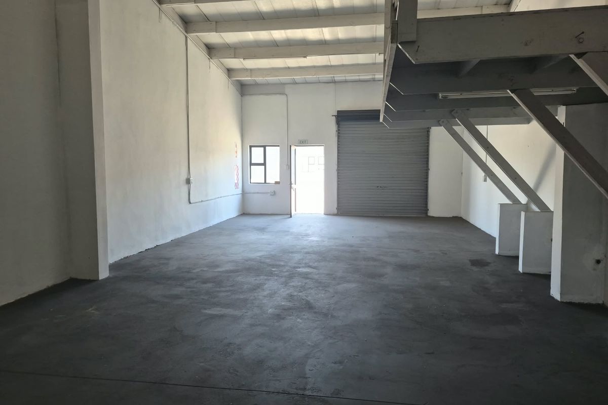 Spacious industrial warehouse unit featuring high ceilings with exposed trusses, a roller shutter door, and a functional mezzanine level for additional storage or office space.
