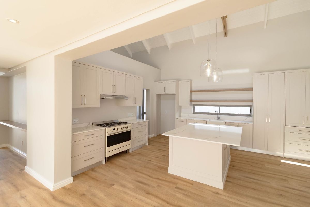 Modern, bright kitchen featuring a central island, gas stove, vaulted ceilings with exposed beams, and high-quality cabinetry with stone countertops.