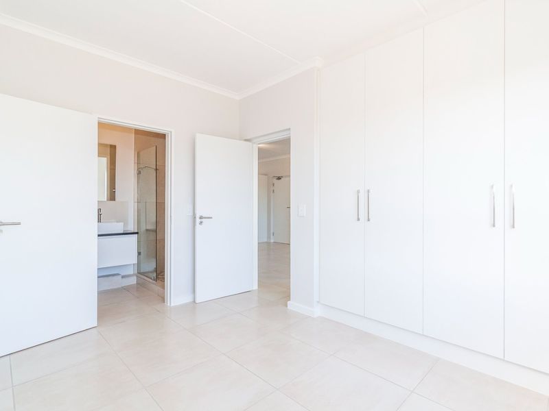 A bright, empty bedroom featuring neutral tiled flooring, ample built-in cupboard space, and direct access to an en-suite bathroom.