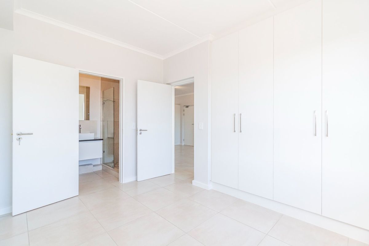 A bright, empty bedroom featuring neutral tiled flooring, ample built-in cupboard space, and direct access to an en-suite bathroom.
