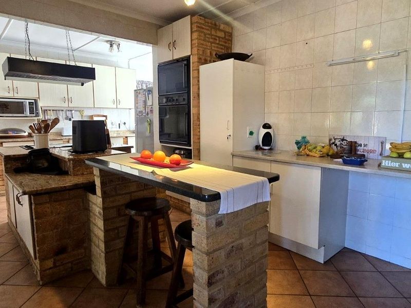 Spacious kitchen featuring brick breakfast bar, granite countertops, built-in oven, and tiled splashbacks, offering a functional layout with ample storage space.